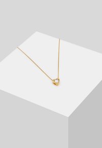 Collana d'oro con pendente a forma di cuore e pietra preziosa trasparente, su una catena fine con una texture liscia.