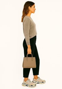 Grijze cropped trui, zwarte broek en beige sneakers. Houdt een kleine tan handtas vast met bovenhandvatten en een gladde textuur.