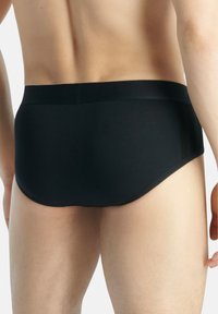 Svarta simbyxor av slätt material, med en låg midja och panelaccenter vid sidorna. Benen har en rundad skärning.