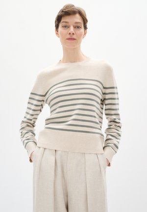 Lys beige pullover sweater med grønne vandrette striber, rund halsudskæring og ribbet kant. Sammen med cremegule linnedbukser.