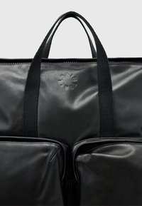 Černá kožená taška se dvěma předními kapsami, horním zipovým uzávěrem a dvojitými krátkými držadly. Má embosované logo uprostřed. Hladký povrch.