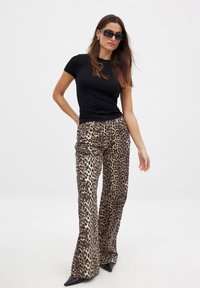 T-shirt noir ajusté associé à un pantalon évasé en imprimé léopard. Les pantalons présentent une texture brillante, une jambe large et des talons noirs pointus.
