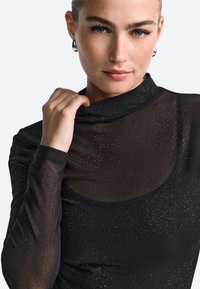 Top negru, cu mâneci lungi și guler înalt, având o textură transparentă decorată cu cristale strălucitoare distribuite aleatoriu pentru un plus de detaliu.