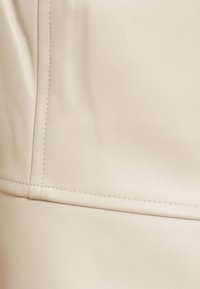 Επιφάνεια από μπεζ συνθετικό δέρμα με ομαλή υφή, που διαθέτει καθαρές ραφές και διακριτική γυαλάδα, παρουσιάζοντας έναν μινιμαλιστικό σχεδιασμό.