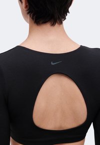 Πίσω όψη ενός ατόμου που φοράει ένα μαύρο τοπ Nike με μεγάλο οβάλ άνοιγμα στην πάνω πλάτη, που αποκαλύπτει γυμνό δέρμα.