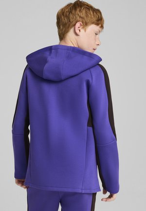 Fioletowa bluza z kapturem z teksturowanym czarnym panelem bocznym, z kapturem, wykonana z gładkiego materiału. Posiada luźny krój i długie rękawy.