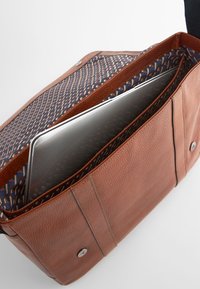 Geantă pentru laptop din piele maro cu exterior texturat, având o căptușeală din material cu model în albastru, roșu și alb, și o închidere magnetică.