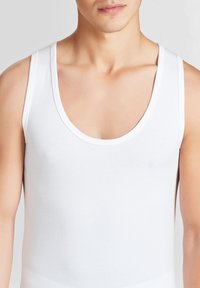 Top in cotone bianco con scollatura rotonda, spalline larghe e una texture liscia. Nessun motivo visibile o dettagli metallici.