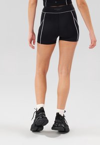 Černé atletické šortky s bílým ozdobným lemem, s vysokým pasem. Nošeny s černými teniskami a bílými ponožkami po lýtka.