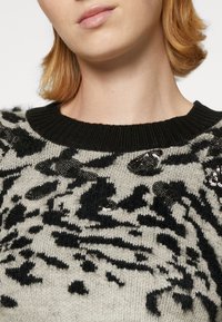 Gray knit sweater with black abstract patterns and sequin accents. Features a ribbed black neckline and soft texture.