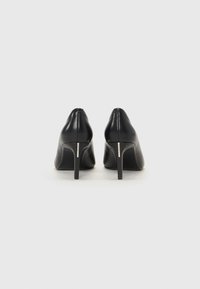 Scarpe con tacco alto in pelle nera, con punta affusolata, dotate di un sottile tacco a stiletto e un accento metallico vicino alla base del tacco.
