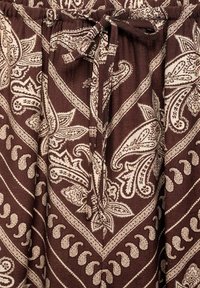 Brown fabric with cream paisley pattern, featuring an elastic waistband and a tied drawstring. Textured with vertical ribbing details.