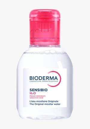Botella de plástico transparente con tapa rosa, que contiene agua micelar. La etiqueta presenta un fondo blanco con texto azul y rosa que detalla el producto.