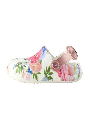 Zueco blanco tipo slip-on con estampado floral multicolor y correa ajustable metálica rosa con botón redondo en el lateral.