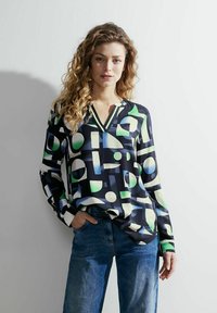 Blusa a maniche lunghe in tessuto blu navy scuro con un motivo geometrico in verde, bianco e blu. Design a V e vestibilità rilassata.
