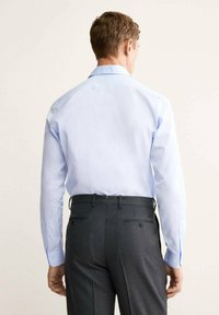 Chemise à manches longues bleu clair avec un col standard, associée à un pantalon gris foncé avec des poches arrière et des passants de ceinture. Design uni, sans motifs.