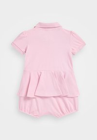 Vaaleanpunainen puuvillainen haalari, jossa on lyhyet hihat, kauluksellinen pääntie ja peplumhelma. Ominaisuuksiin kuuluvat joustavat lahkeensuut ja sileä, teksturoitu kangas.