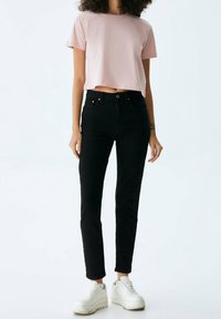 T-shirt cropped rosa, jeans neri a vita alta e sneakers bianche. Tessuto morbido, design aderente e dettagli sottili sulle tasche.