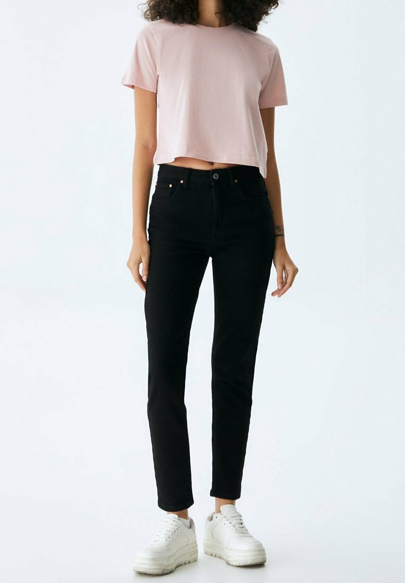 T-shirt cropped rosa, jeans neri a vita alta e sneakers bianche. Tessuto morbido, design aderente e dettagli sottili sulle tasche.