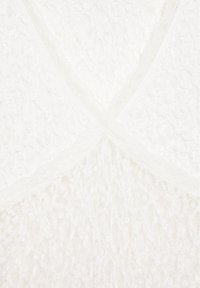 Gros plan sur un tissu en maille blanche avec des motifs texturés en câble et en diamant dans un design entrecroisé.