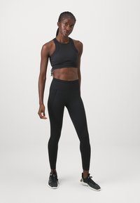 Fekete sportos crop top és magas derekú leggings rugalmas anyagból. A leggings mintás díszítésekkel és kontúrvonalakkal rendelkezik.