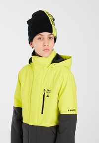 Veste jaune et grise en matériau imperméable ; dotée d'un col haut, d'une poche zippée et d'un logo sur la manche. Bonnet noir avec logo.