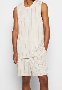 Beige sportig tanktop och shortset i meshtyg med vertikala teal-ränder och en avslappnad design. Fickor i shortsen.