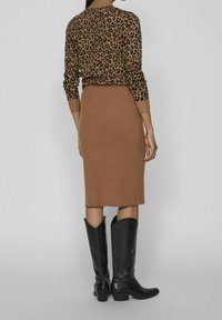 Hnědý svetr s leopardím vzorem a žebrovanou texturou, spárovaný s přiléhavou béžovou sukní a vysokými černými koženými botami s špičatou špičkou a rozšířeným horním dílem.