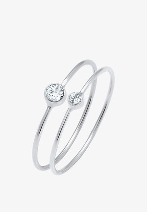 Bague double en argent avec des bandes fines, chacune comportant une pierre précieuse ronde claire, sertie en chaton, de tailles différentes.