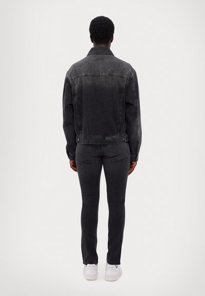 Black denim jacket with a slightly faded finish, featuring a classic collar and button-up closure, paired with matching slim-fit jeans and white sneakers.