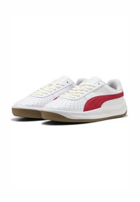 Sneaker atletici bianchi con una striscia rossa sul lato, perforazioni testurizzate sulla punta, lacci color crema e suola in gomma beige.