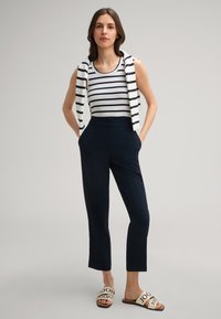 Witte en marineblauwe gestreepte tanktop, marineblauwe op maat gemaakte broek en lichtgekleurde sandalen met logo. Heeft een casual gedrapeerde hoodie.