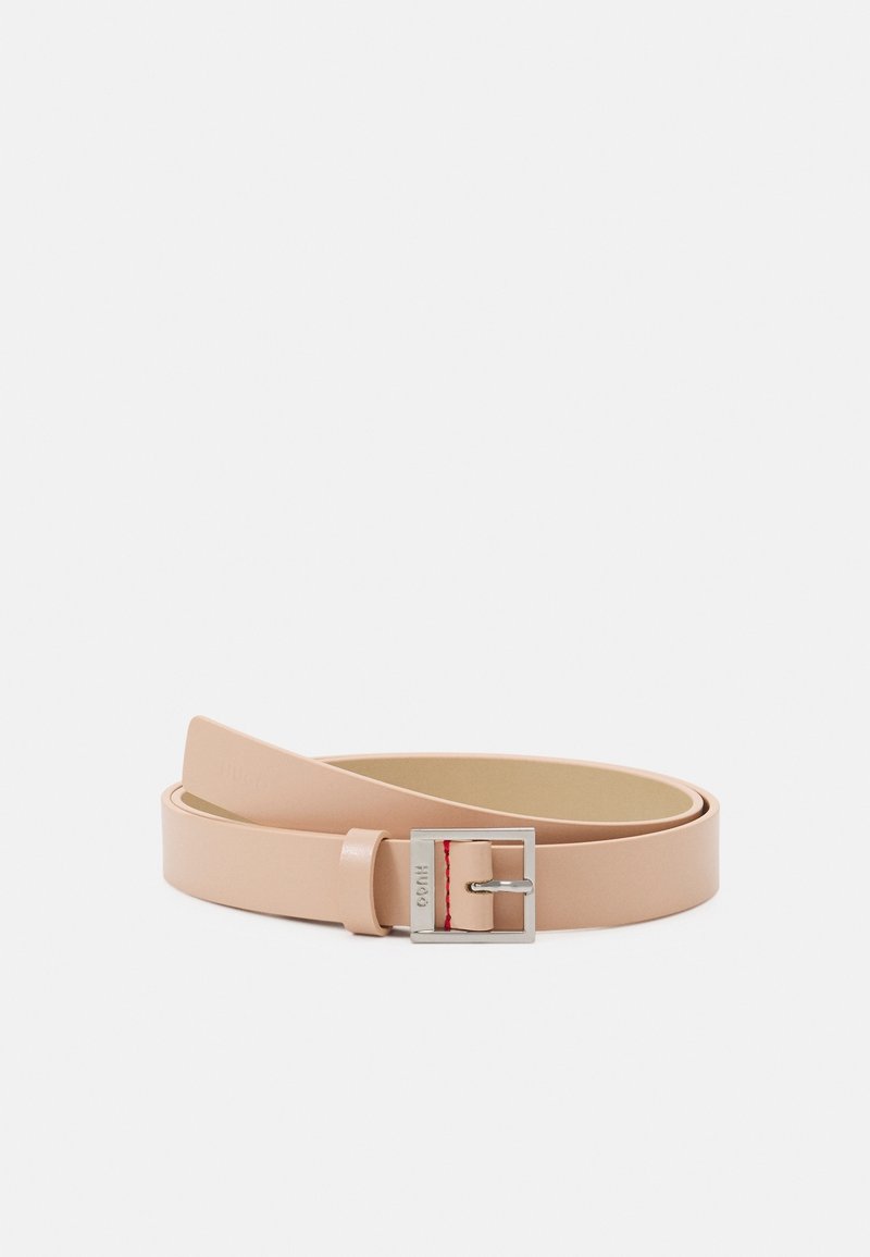 Ceinture en cuir beige clair soigneusement roulée avec une boucle carrée en argent et un petit détail de point rouge près de la fermeture.