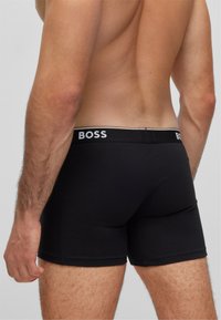 Schwarze Boxershorts mit körpernahem Schnitt, ausgestattet mit einem weißen Logo am Bündchen und einem glatten, elastischen Stoff. 