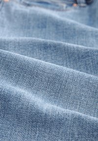 Tissu en denim bleu clair, présentant une texture à tissage fin avec une surface lisse et un léger éclat, plié avec des coutures visibles.