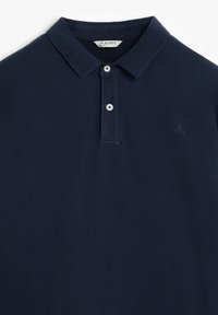 Polo de color azul marino hecho de algodón, con cuello clásico, tapeta de dos botones y un pequeño logo en el pecho. Textura suave.