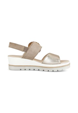 Beige en metallic open-toe sleehak sandaal met klittenbandsluiting bij de enkel en een witte geribbelde zool, vanaf de zijkant weergegeven.