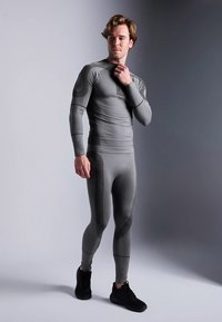 Szürke, testhezálló sportos egyrészes ruha hosszú ujjakkal és texturált díszítéssel. Kerek nyakkivágású és letisztult kialakítású. Fekete cipővel viselve.