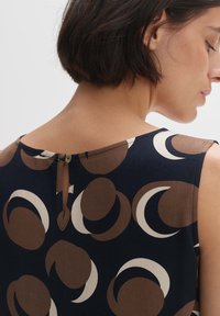 Sleeveless navy dress featuring a circular pattern in brown and cream, with a keyhole back closure and smooth fabric texture.