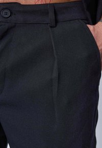 Pantalon noir en tissu lisse avec une coupe droite, doté d'une fermeture à bouton et de plis avant pour une touche de design supplémentaire.