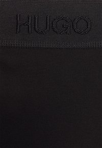 Schwarze Sportshorts mit glatter Textur, ausgestattet mit einem gestickten "HUGO"-Logo auf einem Netzbund.