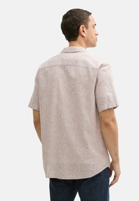 Hellrosa Kurzarmhemd mit strukturiertem Muster, Button-Down-Kragen und Rückenpasse, kombiniert mit dunklen Jeans.