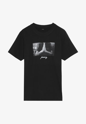 Sort bomulds-T-shirt med korte ærmer, med et grafisk print af sammenknyttede hænder og ordet "pray" i hvid nedenunder.