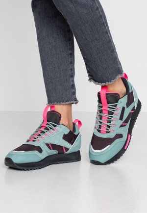 Lichtgroene en zwarte sportschoenen met roze accenten. Suède en mesh materialen, met een textuurzool en robuust ontwerp.