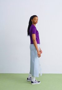 Top morado de manga corta, falda maxi de mezclilla azul clara, combinada con calcetines blancos y zapatillas moradas; textura suave y diseño ajustado.