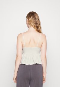 Ljusgrå peplumtop med tunna remmar, strukturerad tyg och utsvängd nederkant, bärs tillsammans med mörkgrå byxor, som visar bakvyn.