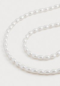 Fio de pérolas ovais brancas dispostas em uma espiral solta sobre um fundo branco liso.