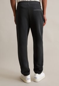 Schwarze Sweatpants mit einem elastischen Bund und einer Gesäßtasche. Der Stoff scheint weich zu sein und hat eine leicht gebürstete Textur. Getragen mit weißen Sneakers.