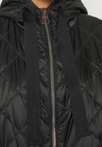 Chaqueta negra acolchada con capucha, que cuenta con un cierre de cremallera de longitud completa y amplias correas de tela con el logo de Marc O'Polo a los lados.