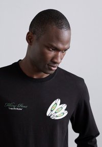 Black long-sleeve shirt featuring a graphic of three stylized pizza slices in white, green, and black, with brand text on the front.